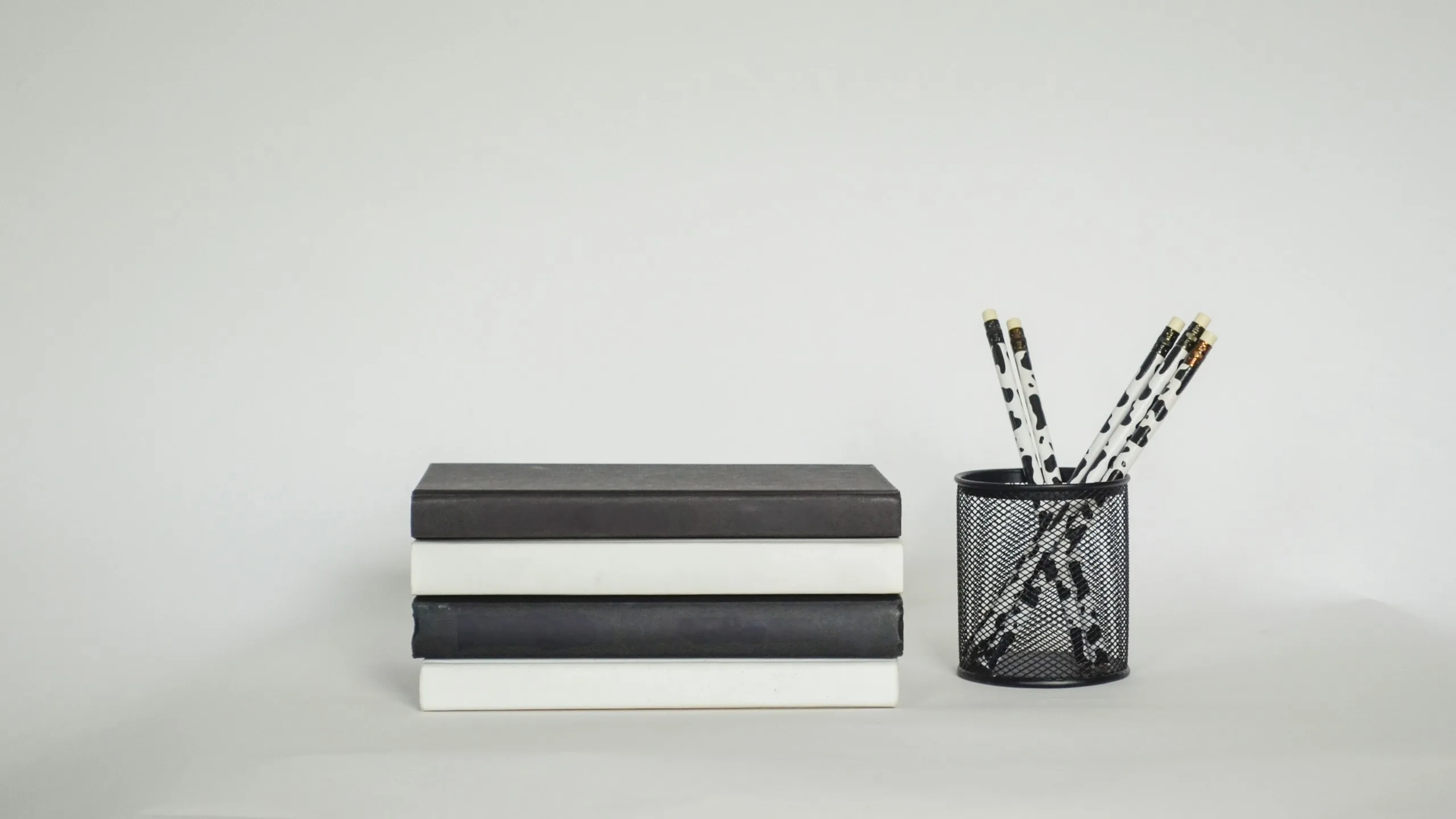 Flat lay kit notebook hitam-putih dan tempat pulpen di atas latar abu-abu terang
